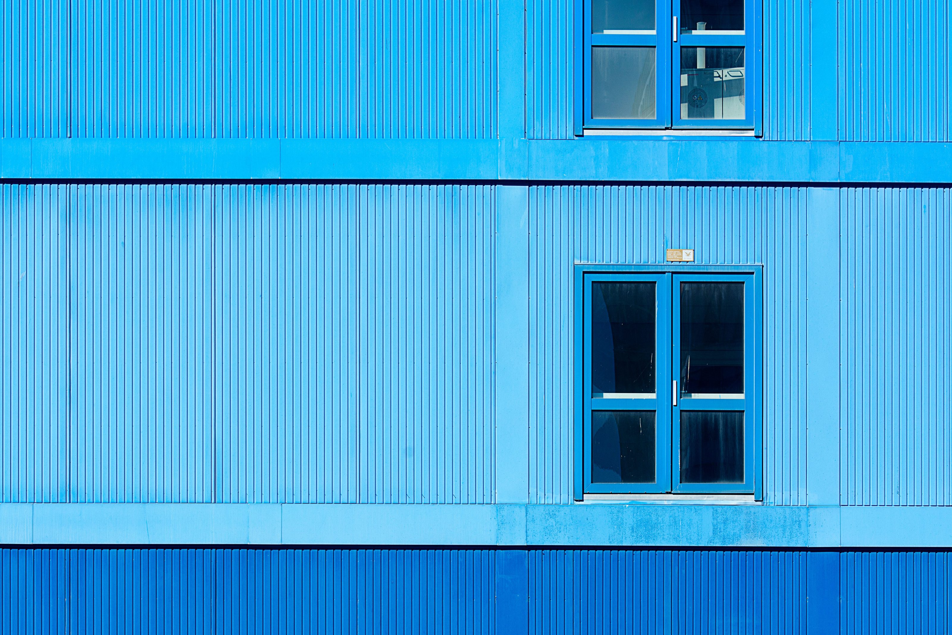 Fachada industrial azul em chapas metálicas com duas janelas